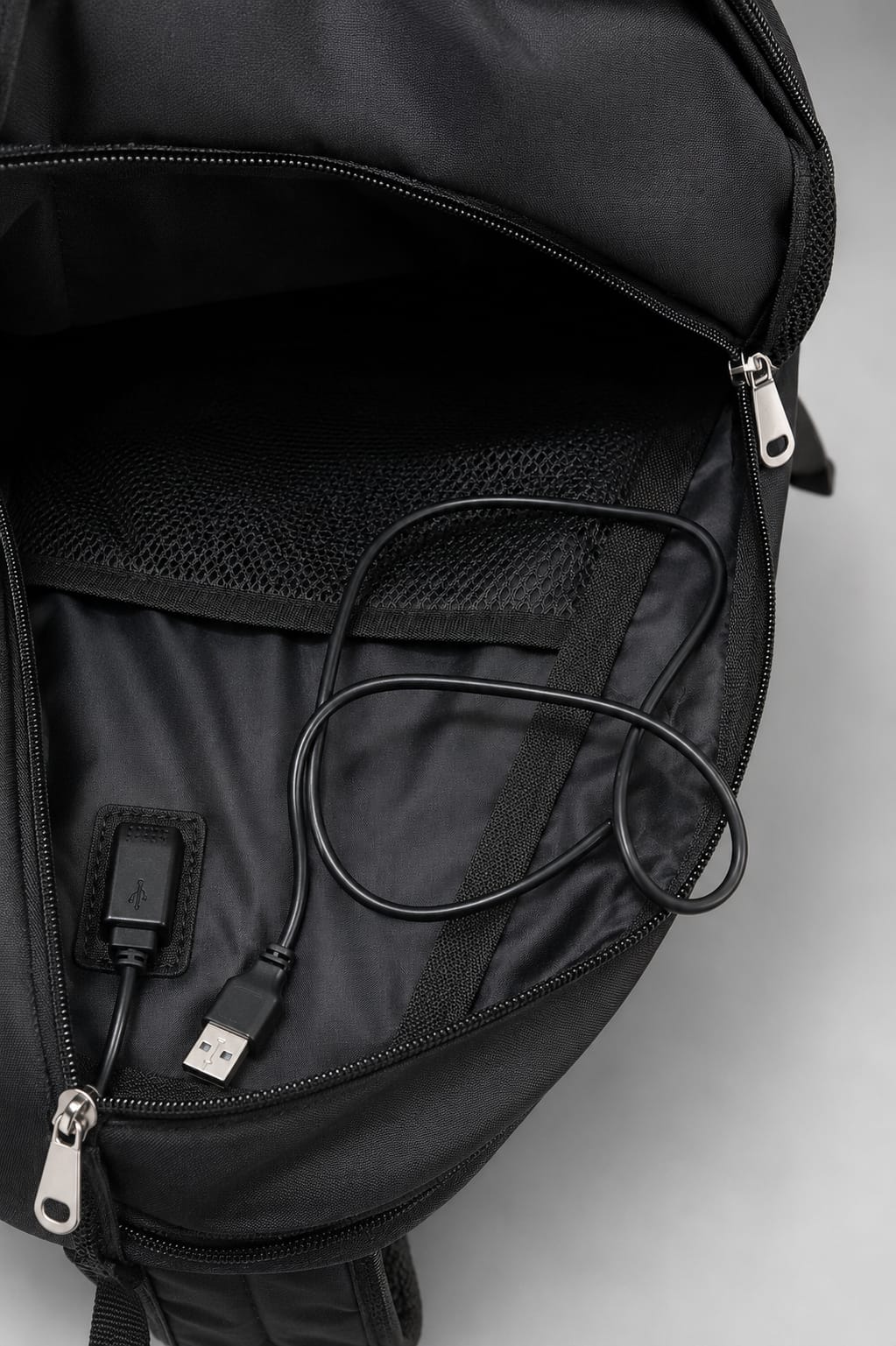 Black backpack with USB cable and charging port on a light gray background