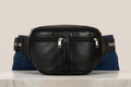 Black leather waist bag on a white surface with a neutral background